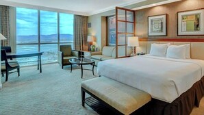 A hotel room with a large bed, a seating area with a table, and a view of the water. - The Signature Studio Suite | Jacuzzi & Full Bath (Las Vegas)