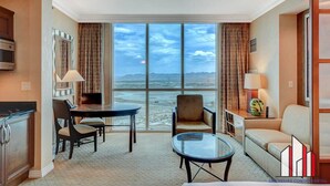 A hotel room with a dining area, a sofa, a glass table, and a view of the beach. - The Signature Studio Suite | Jacuzzi & Full Bath (Las Vegas)