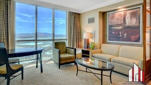 Une chambre d’hôtel dotée d’une grande fenêtre donnant sur le paysage urbain, d’un canapé, d’un fauteuil, d’une petite table et d’une lampe.