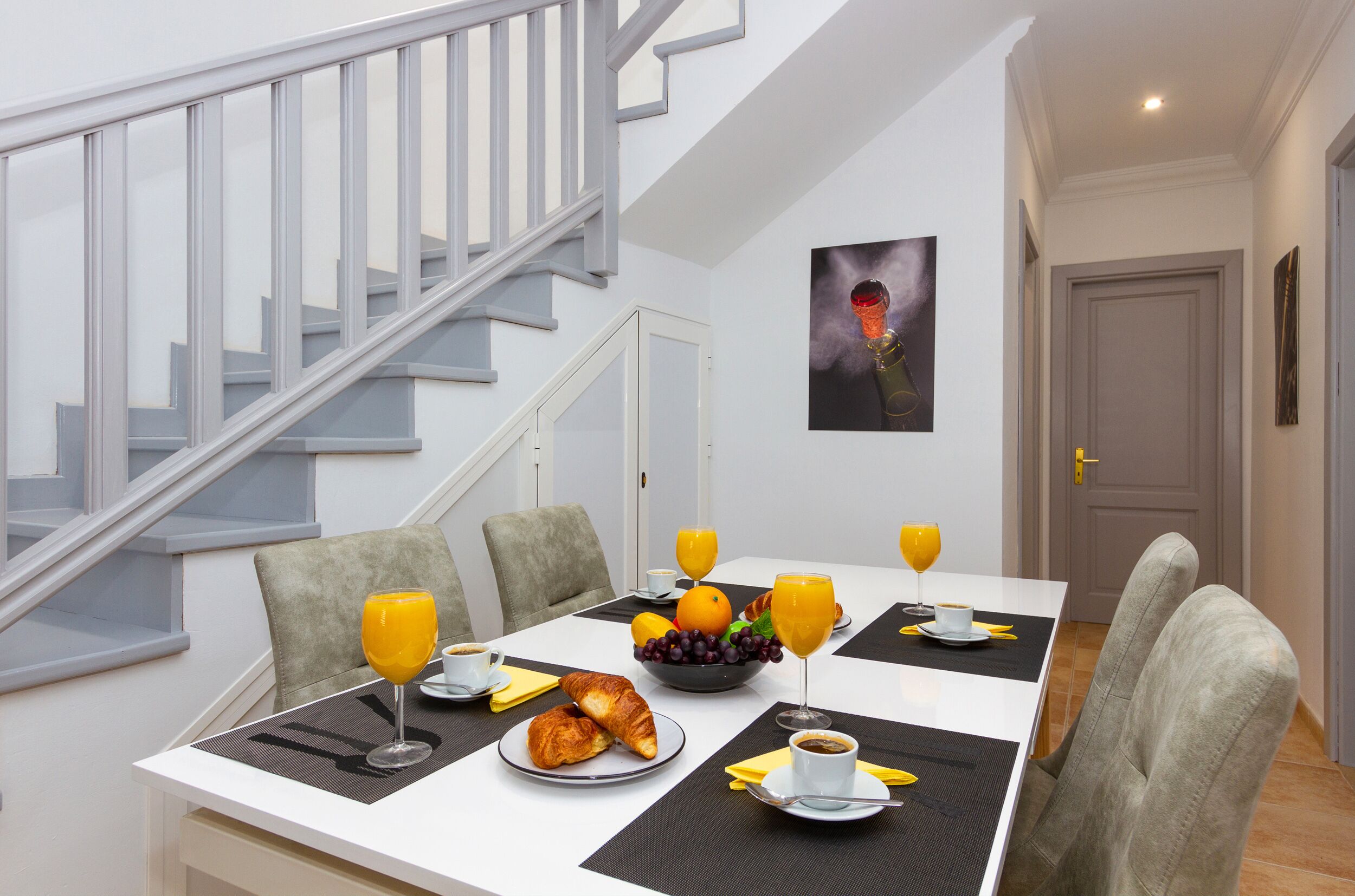A dining area with a table set for breakfast, including croissants, fruit, and orange juice.
