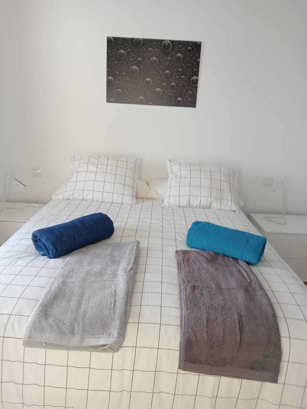 A bed with a grid-patterned bedspread, two pillows, and three folded towels in blue, gray, and brown.