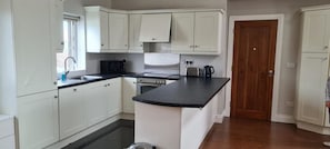 A kitchen with white cabinets, a black countertop, a stove, and a sink.