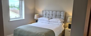 Ein Schlafzimmer mit einem Bett, zwei Nachttischen, einem Fenster und Blick ins Freie.