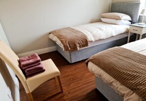 A bedroom with a bed, a chair with a towel, a bedside table, and a nightstand.