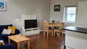A living room with a sofa, a coffee table, a fireplace, and a dining area with chairs and a table. - Carraroe Apartment 2 Modern apartment in Carraroe (Carraroe)