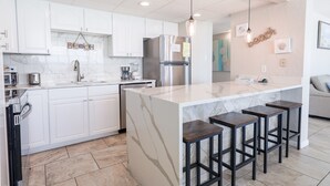 Una cocina moderna con armarios blancos, una isla de mármol y taburetes de bar.