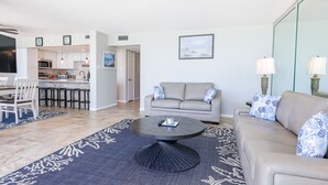 Una sala de estar moderna con una mesa redonda, un sofá y un comedor con sillas, y una cocina al fondo.