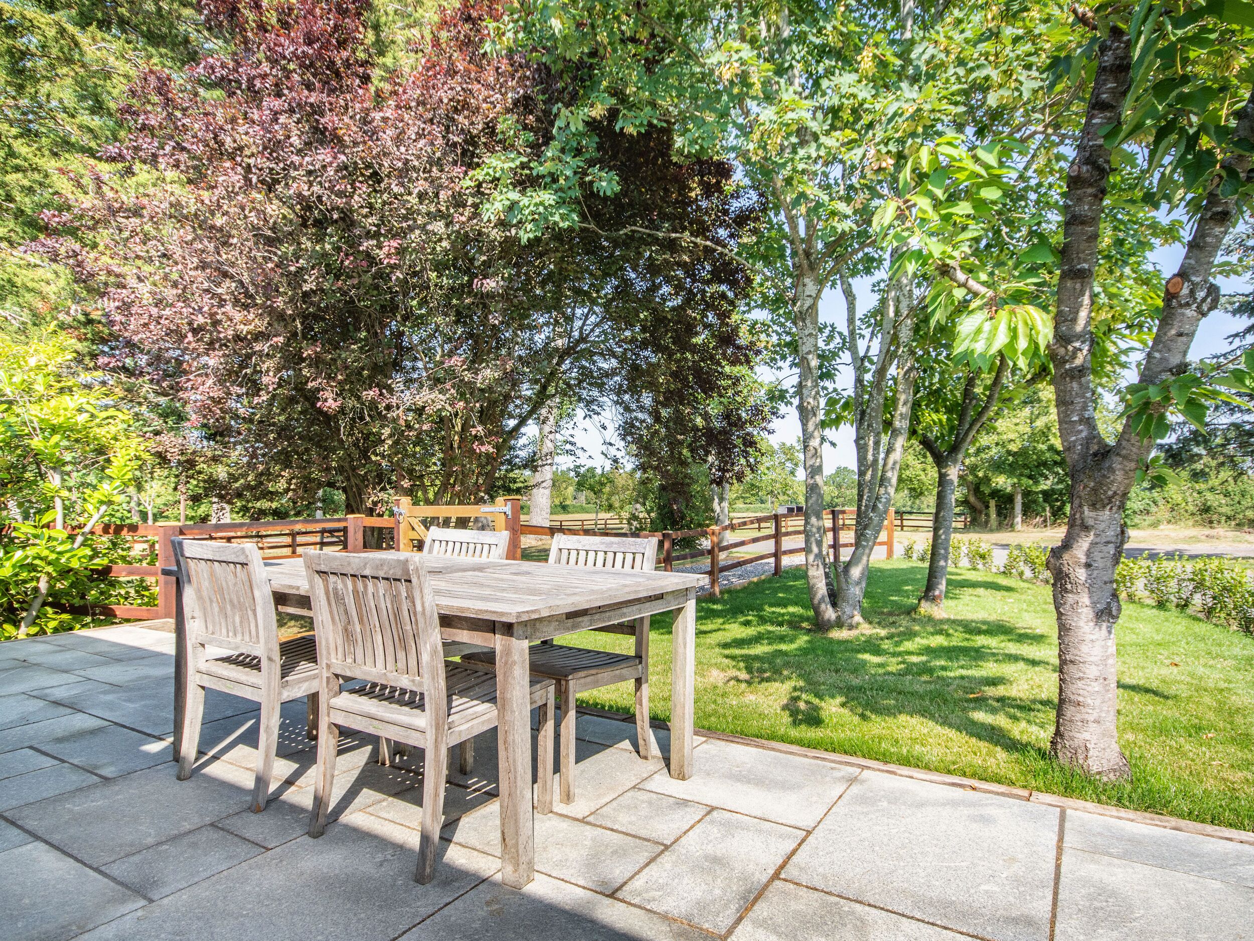 Un patio al aire libre con una mesa y sillas de madera, rodeado de exuberante follaje y árboles.