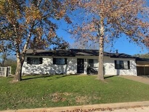 Ein eingeschossiges Haus mit weißer Fassade, einer Veranda und einer Garage.