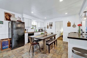 A modern kitchen with white cabinets, a black refrigerator, a wooden dining table, and a bench.