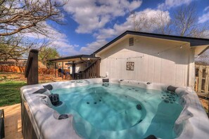 A hot tub in a backyard with a covered patio and a white building in the background.