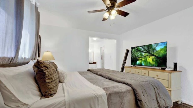 Une chambre avec un lit, un ventilateur de plafond, une télévision et une commode.
