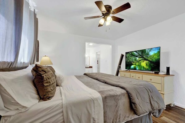 Ein Schlafzimmer mit Bett, Deckenventilator, Fernseher und Kommode.