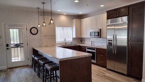 A modern kitchen with a central island, stainless steel appliances, and a wooden floor.