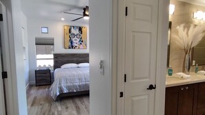 A bedroom with a bed, bedside tables, a ceiling fan, and a painting on the wall.