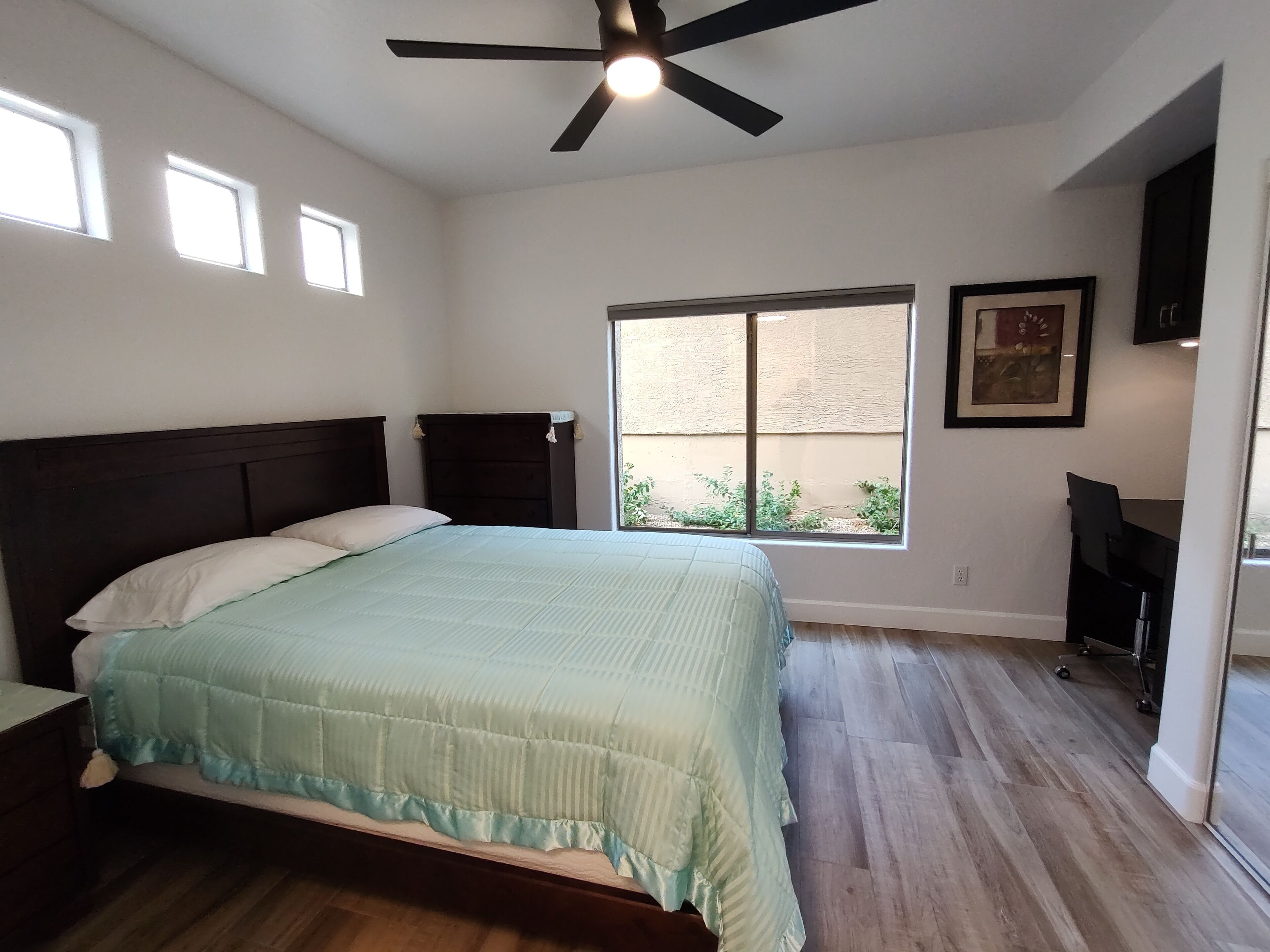 A bedroom with a bed, a ceiling fan, a window, and a desk.