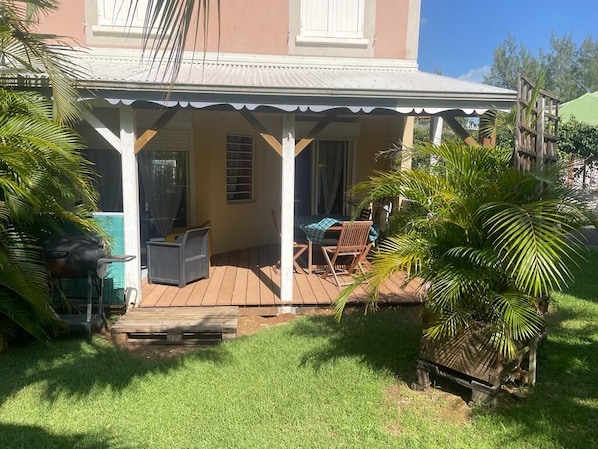 A covered porch with a grill, chairs, and a small table.