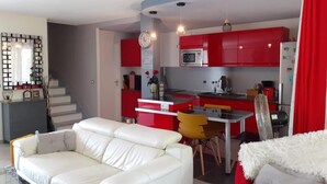 Un saló modern amb un sofà blanc, una zona de menjador amb armaris vermells i una cuina amb armaris vermells i un microones.