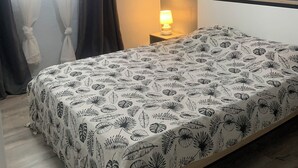 Un dormitori amb un llit, una tauleta de nit, una làmpada, un aparell d'aire condicionat i una finestra amb cortines.