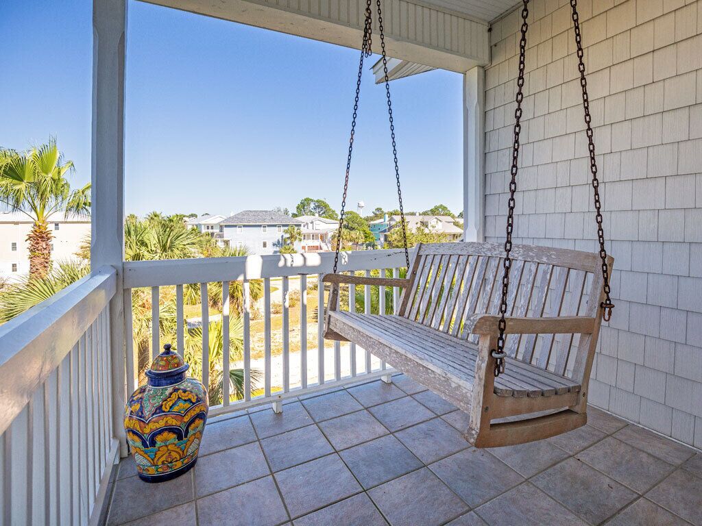 Un balcon agrémenté d’une balançoire en bois, d’un vase décoratif et offrant une vue sur des palmiers et des maisons.