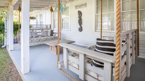 A porch with a swing set, a bench, and a decorative wall. - Beach Bum Inn by Tybee Vacation Rentals (Tybee Island)