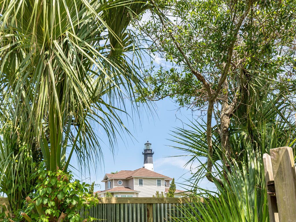 Une maison avec un phare en arrière-plan, entourée d’une végétation luxuriante.