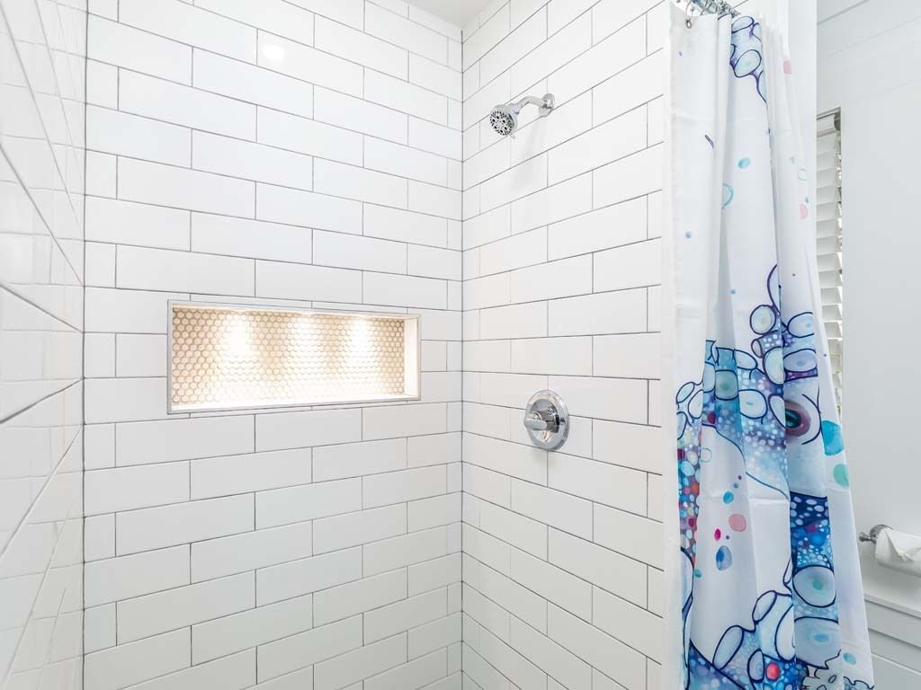 A shower with white tiled walls, a glass-enclosed showerhead, and a colorful shower curtain.