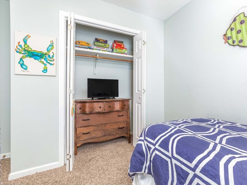 A bedroom with a bed, a television on a wooden dresser, a shelf with books, and a painting on the wall.