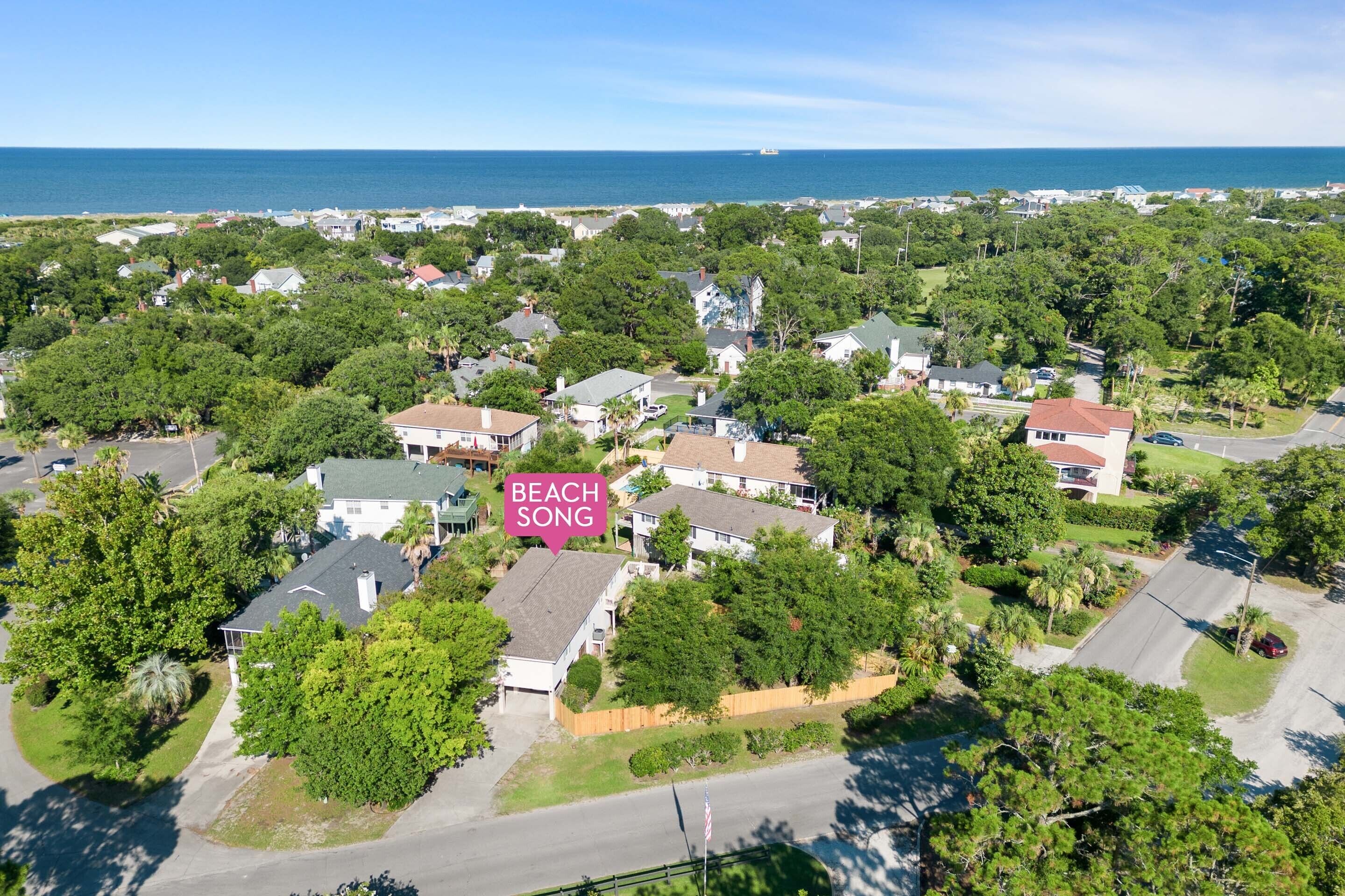 An aerial view of a residential area with houses, trees, and a beach in the background.