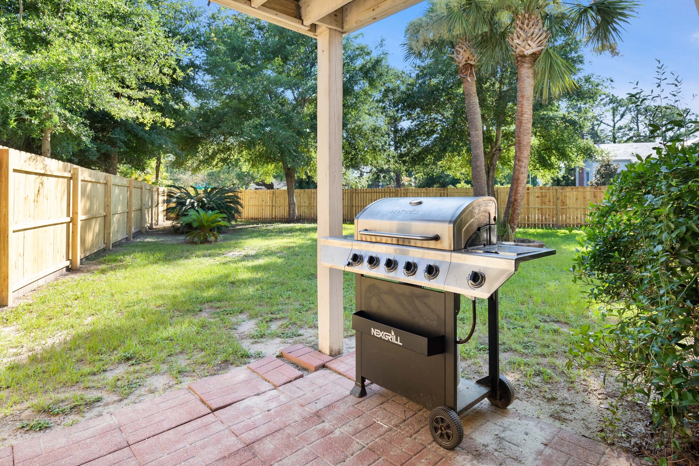 A portable grill with multiple burners and a storage drawer, set up on a brick patio.