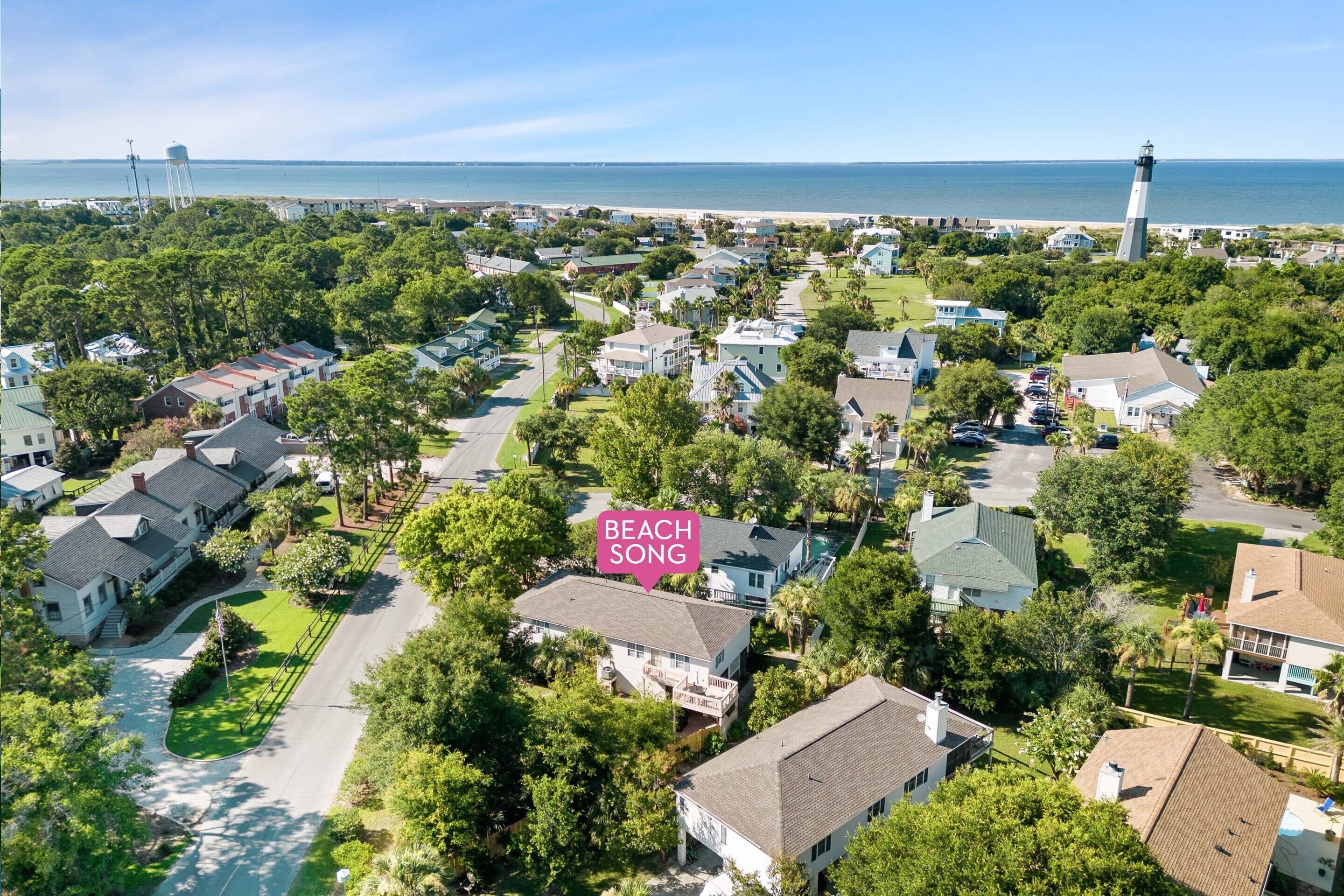 An aerial view of a residential area with houses, trees, and a lighthouse in the distance.