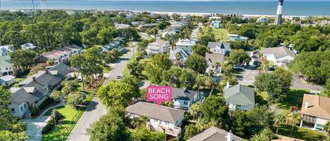 An aerial view of a residential area with houses, trees, and a lighthouse in the distance.
