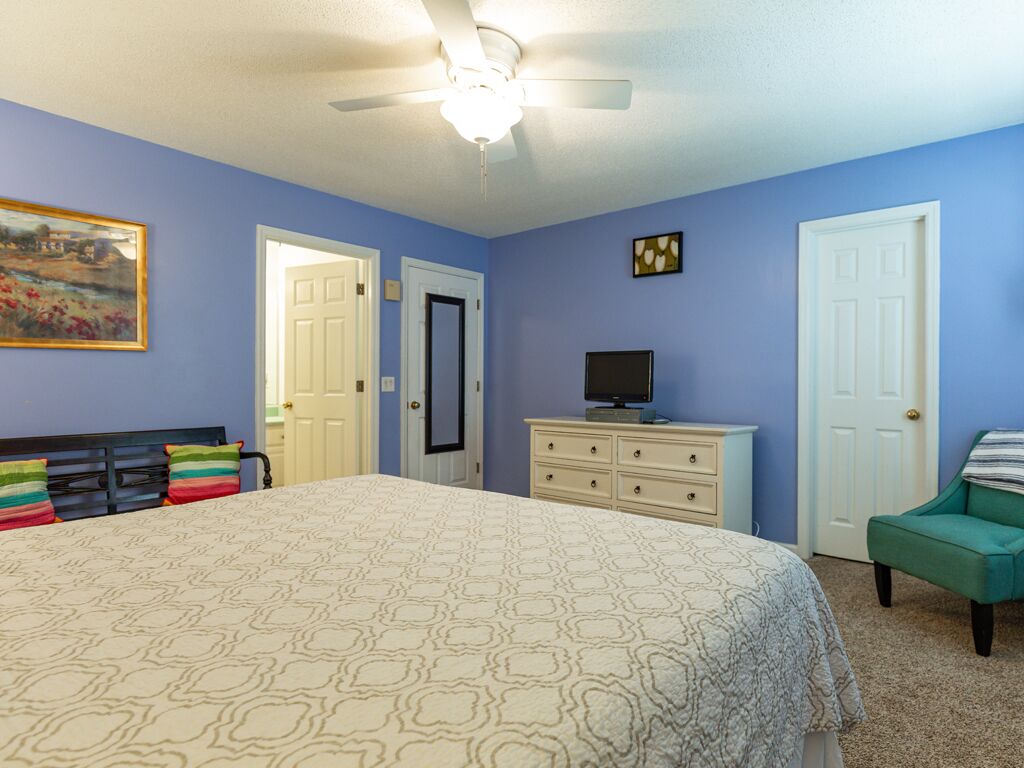 Ein Schlafzimmer mit Bett, Schminktisch, Fernseher und Deckenventilator.