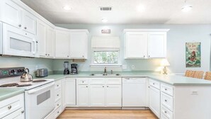 Une cuisine avec des meubles blancs, une cuisinière, un four à micro-ondes et un évier.