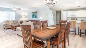 Un vaste salon doté d’une grande table à manger en bois, de sièges confortables et d’un coin cuisine à l’arrière-plan.