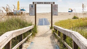 Une passerelle en bois mène à North Beach, où se trouvent des panneaux indiquant les règles à respecter sur la plage et un drapeau signalant la présence d’un sauveteur.