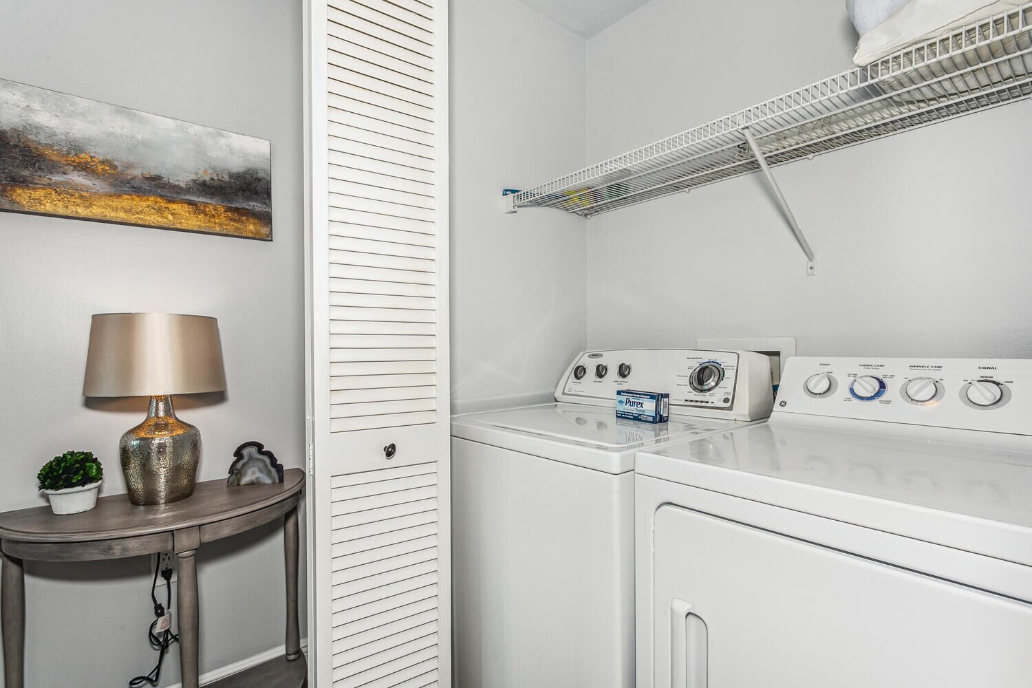 Une buanderie équipée d’un lave-linge, d’un sèche-linge et d’une étagère sur laquelle se trouve une boîte de lessive Purex.