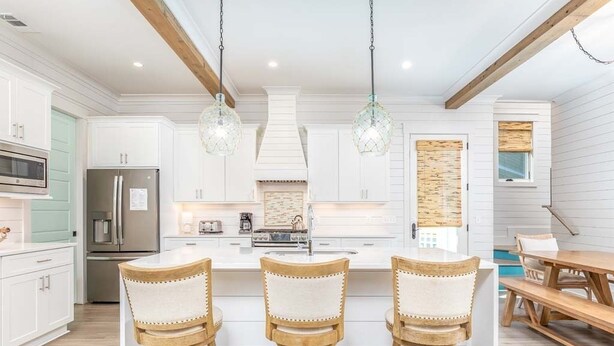 A modern kitchen with white cabinets, a central island with bar stools, and pendant lighting. - Big Wave by Tybee Vacation Rentals (Tybee Island)