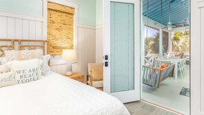 A bedroom with a bed, a nightstand, a chair, and a sliding glass door leading to an outdoor area with a table and chairs. - Big Wave by Tybee Vacation Rentals (Tybee Island)