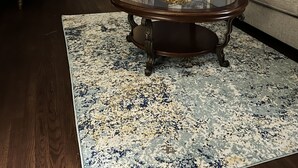 A living room with a round glass coffee table, a sofa, a chair, and a large window with curtains.