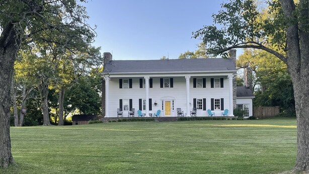 A large white house with a front porch, multiple windows, and a well-maintained lawn.
