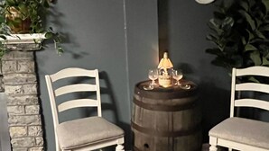 A room with two white chairs, a wooden barrel, a small table with a candle, and a stone fireplace.