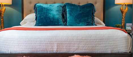 Una cama con cabecera capitonada, dos almohadas color turquesa y una colcha blanca y roja.