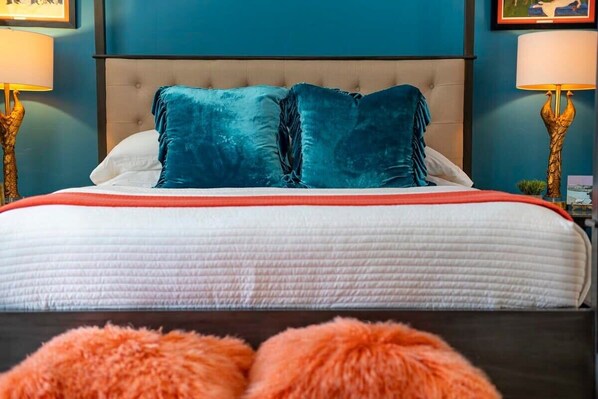 Una cama con cabecera capitonada, dos almohadas color turquesa y una colcha blanca y roja.