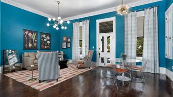 Een kamer met een blauwe wand, een houten vloer, een eettafel met stoelen, een bank, een decoratieve plaid en een kroonluchter.