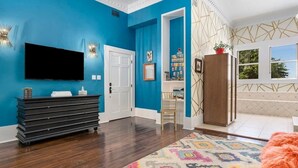 Una stanza con una parete blu, una TV a schermo piatto montata sopra un mobile nero, un tappeto decorato e un armadio in legno.