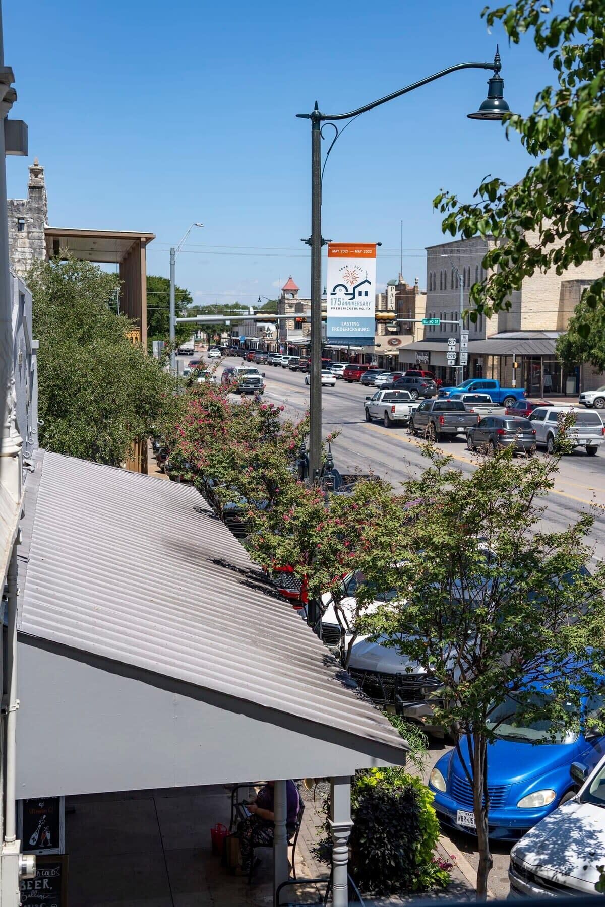 Vista de la calle con automóviles estacionados, un edificio con techo metálico y un cartel anunciando un aniversario.