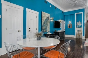 A dining area with a round table and chairs, a peacock painting, and a television on the wall. - The Loft on Main St, Balcony Views, Roman bathtub! (Fredericksburg)