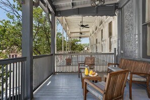 A covered outdoor patio with wooden furniture, a table set with breakfast, and decorative columns. - The Loft on Main St, Balcony Views, Roman bathtub! (Fredericksburg)