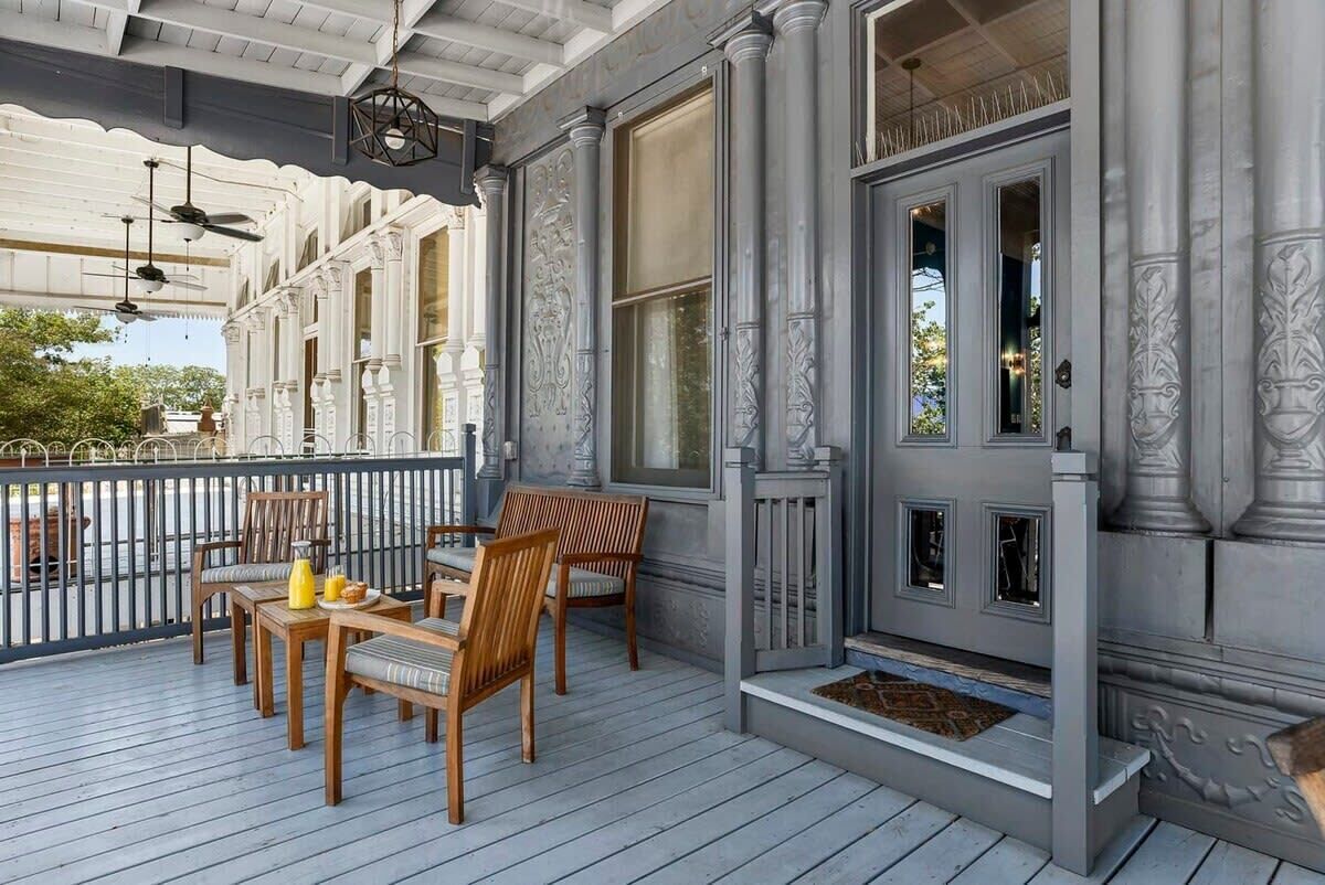 Een overdekt terras met houten meubels en een decoratieve deur.